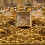 Close-up of gold wedding rings and a delicate tiara on an ornate golden background, symbolizing luxury and elegance.