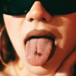Close-up of a fashionable woman sticking her pierced tongue out while wearing sunglasses.